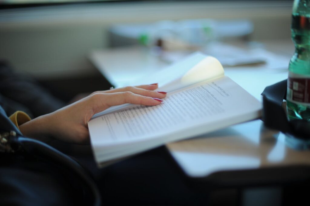 A woman with manicured nails is reading a book at a desk, emphasizing study and relaxation.