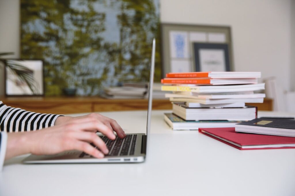 A person typing on a laptop surrounded by stacks of books, ideal for themes of studying and remote work.