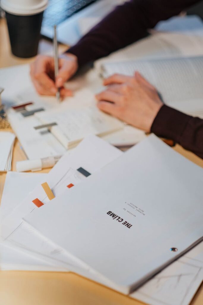 A person engaged in writing notes on a cluttered desk with documents.